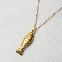 Load image into Gallery viewer, Gold fish-shaped pendant on a chain against a light gray background