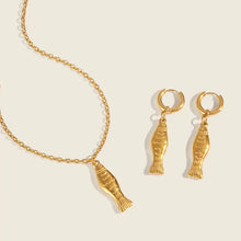Load image into Gallery viewer, Gold fish-shaped necklace and earrings on a beige background
